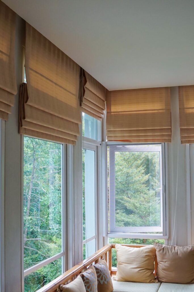 Beige Roman shades over long windows with sun shining in.